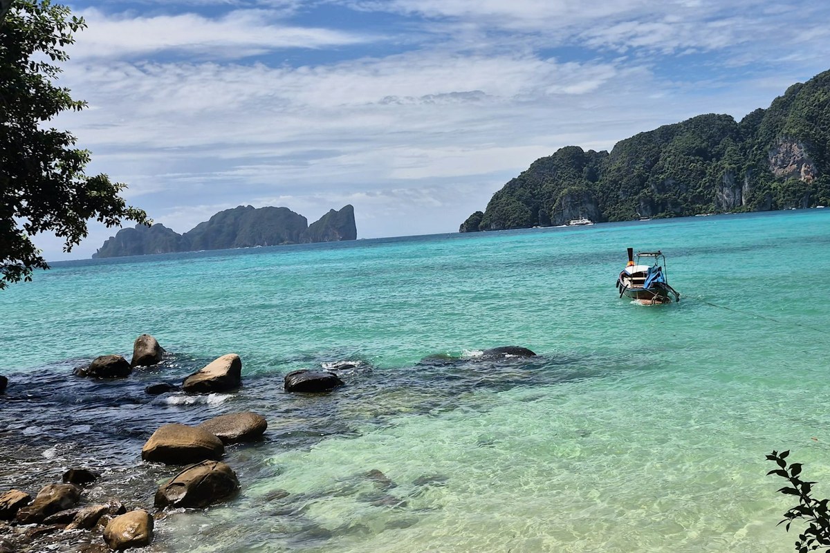 A long-tail boat anchored in turquoise water near rocky islands in Koh Phi Phi
